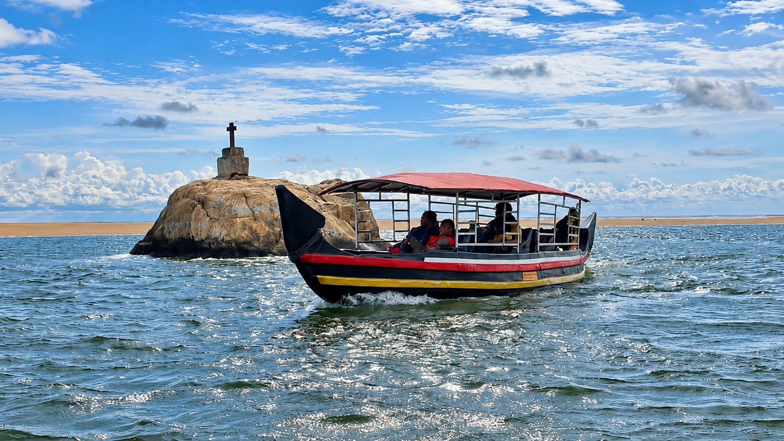 Poovar boat cruising past the rock with the cross near the golden sand beach
